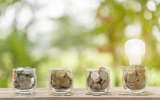 White light bulb and coin in clear jar on wooden table. Money savings for cost of energy concept photo