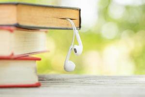 Book and white earphone on wooden table with abstract green nature blur background. Reading and education concept photo