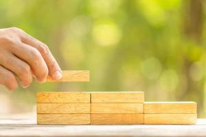 Hand holding blocks wood to make step grow up on green blur background with copy space for text or design concept for business concept photo