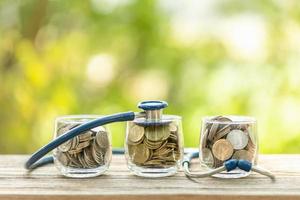 Blue stethoscope and jar of coin on wooden table. Money and financial checking concept photo