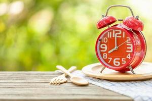 Red alarm clock, Fork, and spoon on wooden table with green outdoor nature blur background. Eight o'clock, Time for eating concept photo