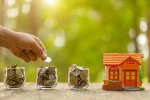 Hand put the coin to piggy bank Home Model on green nature blur background. Money savings concept photo