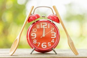 Red alarm clock, Fork, and spoon on wooden table with green outdoor nature blur background. Eight o'clock, Time for eating concept photo