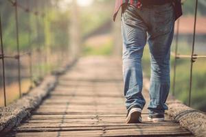 turista asiático caminando por el viejo y roto puente de madera foto