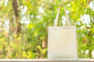 bolsa de algodón blanco puesta sobre una mesa de madera con espacio para texto o publicidad. la bolsa de algodón se puede usar para ir de compras y reemplazar la bolsa de plástico en la naturaleza verde foto