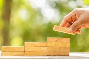 Hand holding blocks wood to make step grow up on green blur background with copy space for text or design concept for business concept photo