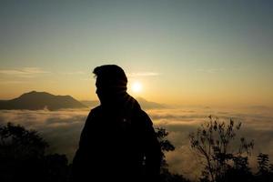 Asian man with background of Sea of Fog covers and golden sunrise the area on the top of hill Doi Phu Thok, Chiang Khan, Loei, Thailand. photo