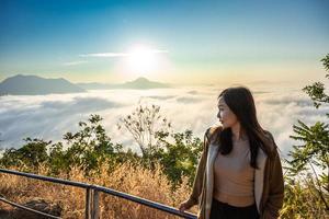 Asian woman with background of Sea of Fog covers and golden sunrise the area on the top of hill Doi Phu Thok, Chiang Khan, Loei, Thailand.