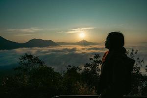 Asian woman with background of Sea of Fog covers and golden sunrise the area on the top of hill Doi Phu Thok, Chiang Khan, Loei, Thailand. photo