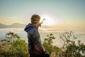 Asian man with background of Sea of Fog covers and golden sunrise the area on the top of hill Doi Phu Thok, Chiang Khan, Loei, Thailand. photo