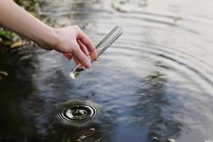 Scientist and biologist hydro-biologist takes water samples for analysis outdoors. Hand is collects water in a test tube. Pond water pollution concept. photo