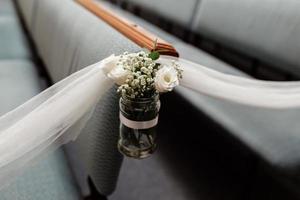 decoración floral blanca en tarro de cristal de sillas en una ceremonia de boda en el interior. foto