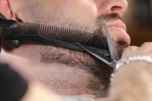 corte de pelo de la barba de un hombre en una peluquería. el maestro barbero profesional afeita la barba del cliente con unas tijeras. hombres barberos. concepto de publicidad y peluquería. enfoque selectivo foto