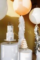 decoración para el primer cumpleaños con pastel de dos pisos y grandes globos blancos y beige con oropel. barra de caramelo con macarrones o macarons. fiesta de cumpleaños. enfoque selectivo foto