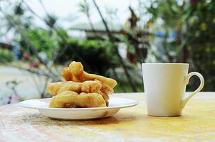 Close up of Patongko deep fried dough stick and white coffee cup on table photo