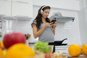 Pregnant Woman Wearing Headphone And Using Smartphone in Kitchen photo