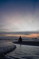 Silhouette of Man Meditate on Beach at Sunset photo