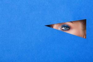 hermosa mujer joven en un agujero en papel azul, hermoso maquillaje brillante. foto