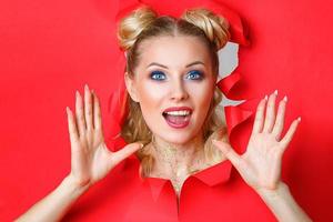 beautiful girl in Peeps out of the hole in red paper, beautiful bright make-up, facial expressions of surprise and interest. photo