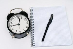 Notepad with alarm clock and pen on a white background. photo