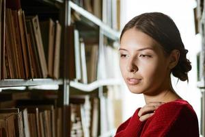 Young woman looks to the side against the background of bookshelves. photo