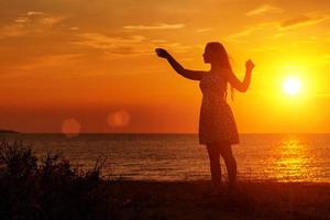 silueta femenina al atardecer en la playa, manos arriba foto