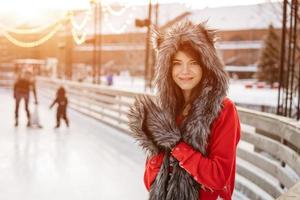 mujer joven feliz en un sombrero de lobo en invierno en la pista de hielo