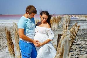 joven hermosa pareja casada, mujer embarazada vestida de blanco en la naturaleza, padres felices esperando al bebé. foto