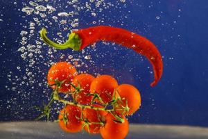 tomates y pimientos rojos flotan en el agua sobre un fondo azul foto