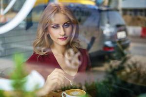 beautiful woman sitting by the window in a cafe drinking coffee. photo