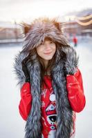 Happy young woman in wolf hat in winter on the ice rink posing in a red sweater photo