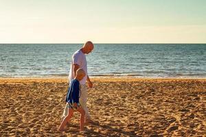 padre e hijo caminan por la playa al atardecer, familia de vacaciones de verano foto