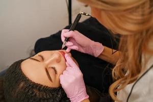 tattoo master makes the client tattoo eyebrows and lips photo