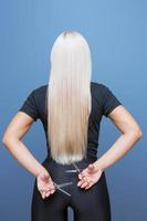 A woman with a pair of scissors stands back and cuts her long blond hair. photo