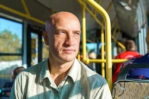 Bald caucasian man rides in public transport while sitting by the window photo