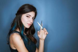 Beautiful brunette woman with a smile cutting long hair with scissors on a blue photo