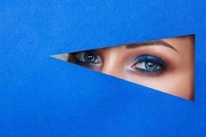 beautiful young woman in a hole in blue paper, beautiful bright make-up.