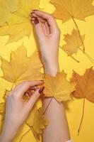 hermosas manos de mujer sobre fondo amarillo de papel, concepto de cuidado de manos de otoño foto