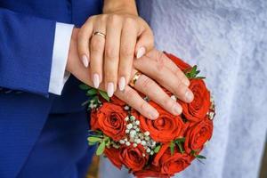manos con anillos de boda en el ramo de la novia foto