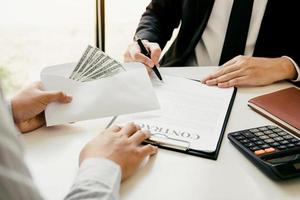 Entrepreneurs are signing a contract about business under fraud while colleagues give money in an envelope. photo