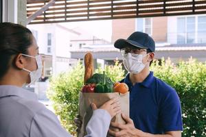 entrega de un hombre asiático con una máscara protectora durante un virus epidémico mientras entregaba una bolsa de comida vegetal a una clienta en la puerta. foto