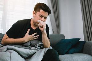 Asian people are sick or ill with bronchitis while coughing by covering their mouth with tissue paper when he sit on the sofa at home. photo