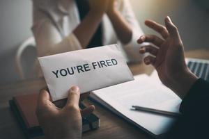 Male manager is talking or explaining about having to dismiss the employee while being handed out a resignation envelope to the employee. photo