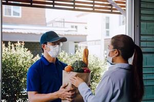 entrega de un hombre asiático con una máscara protectora durante un virus epidémico mientras entregaba una bolsa de comida vegetal a una clienta en la puerta. foto