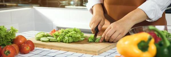 Asian woman uses a knife to cut the salad greens in the kitchen.
