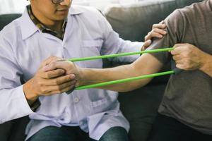 Patient doing stretching exercise with a flexible exercise band and a physical therapist hand to help in clinic room. photo