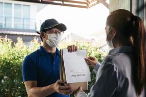 entrega de un hombre asiático que entrega una bolsa de comida a una clienta en la puerta mientras usa una máscara protectora durante una epidemia de virus. foto