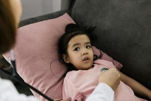 Asian little girl a woman slept in a pillow on the sofa for a female doctor using stethoscope on a heartbeat at home. photo