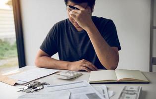 los hombres asiáticos están estresados por problemas financieros, con facturas y calculadoras colocadas sobre la mesa mientras tienen estrés por problemas con los gastos del hogar. foto