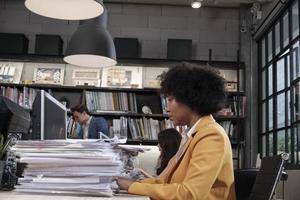 Busy female worker, young African American staff is hard working with a lot of stack of documents and paperwork on desk, overload worked tirelessly for the job deadline in business office workspace. photo